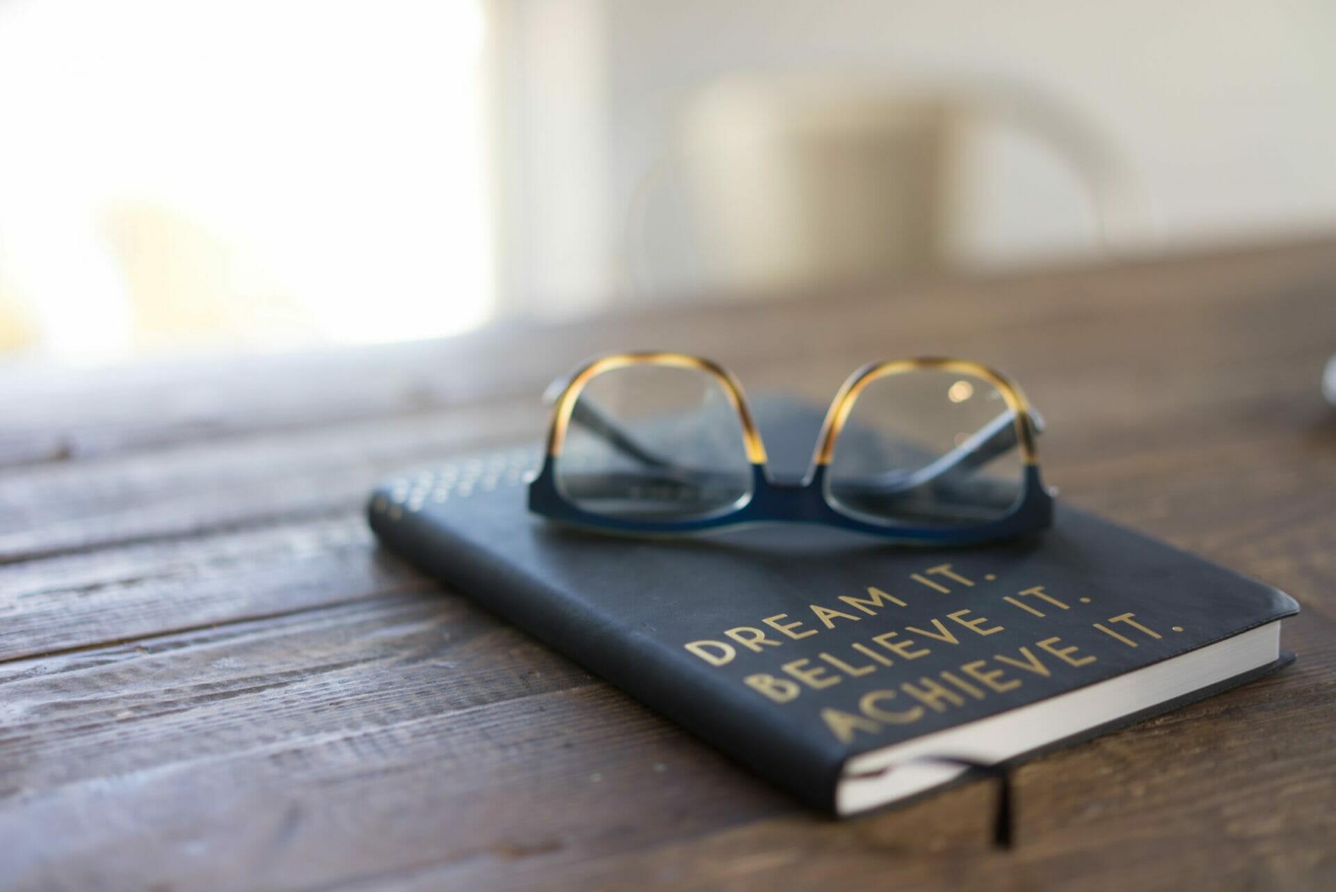 Eyeglasses laying on top of Journal - How to Dream the “Impossible” Dream … And Prioritize It.