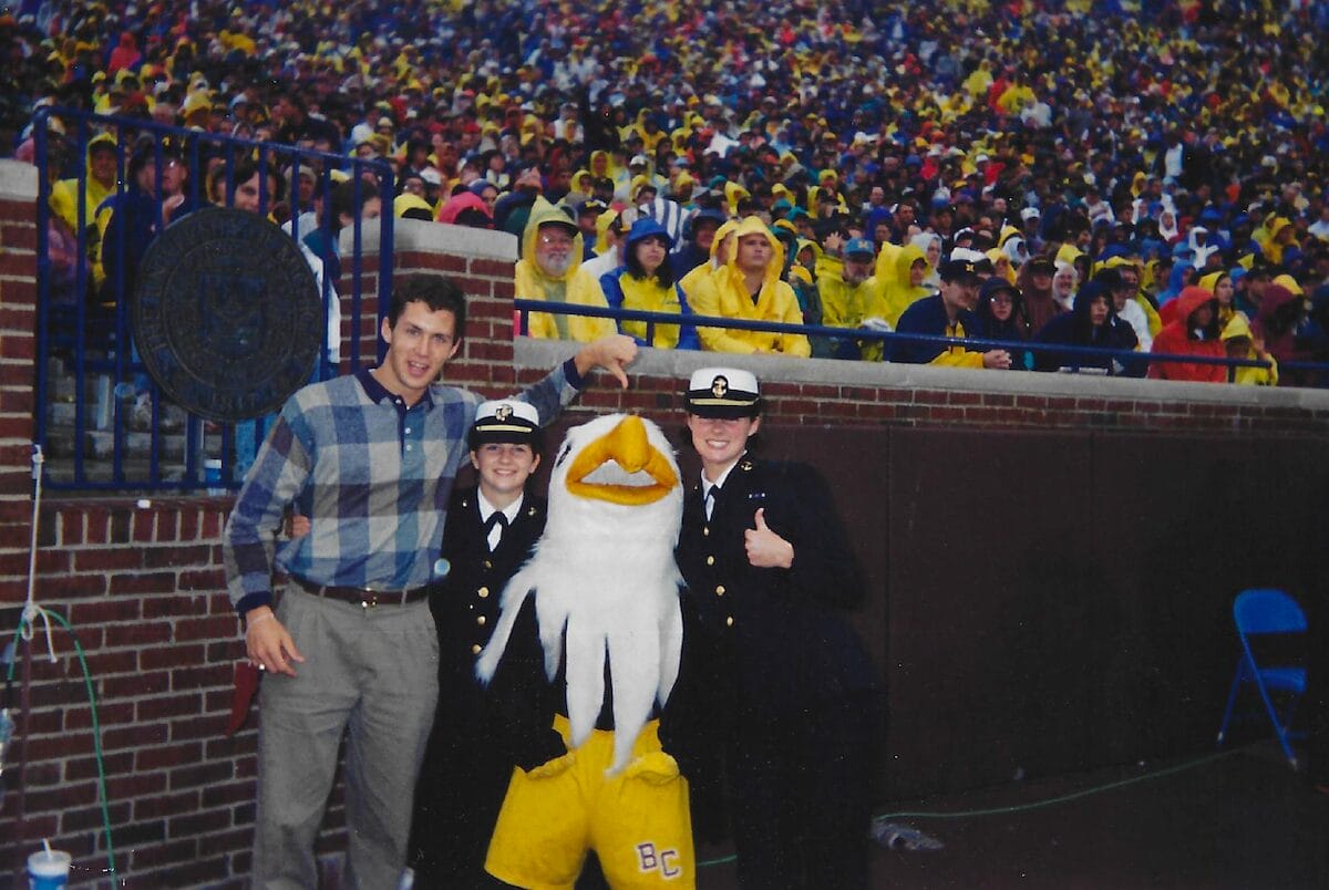 young Angie Witkowski standing next to a mascot on the football sidelines during a game