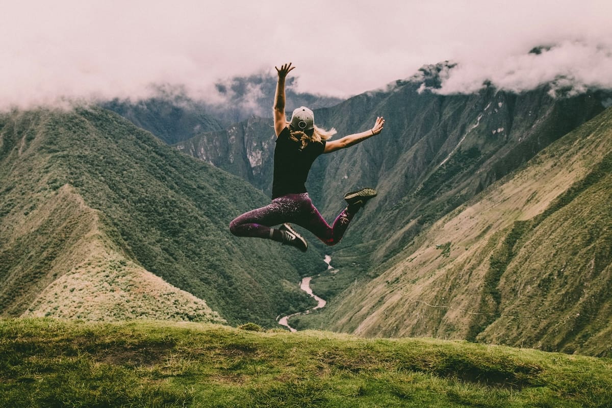 Woman jumping with her hands in the air at the top of a mountain