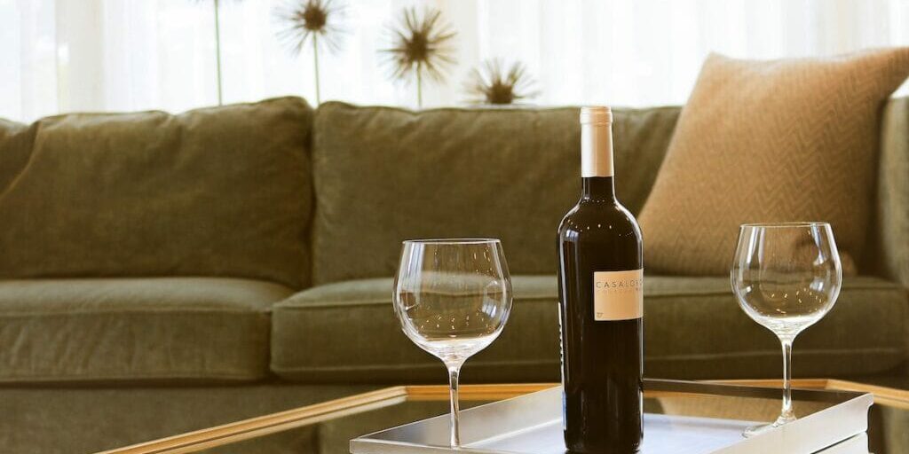 Two empty glasses of wine sitting on a coffee table next to an unopened bottle of wine