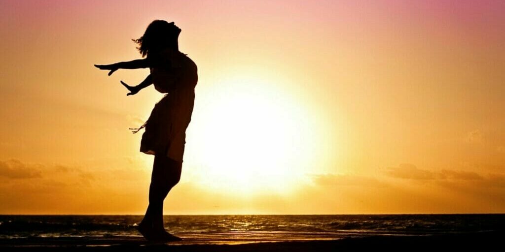 Woman feeling the sea air at the beach at sunset - Build Your Confidence One Moment at a Time
